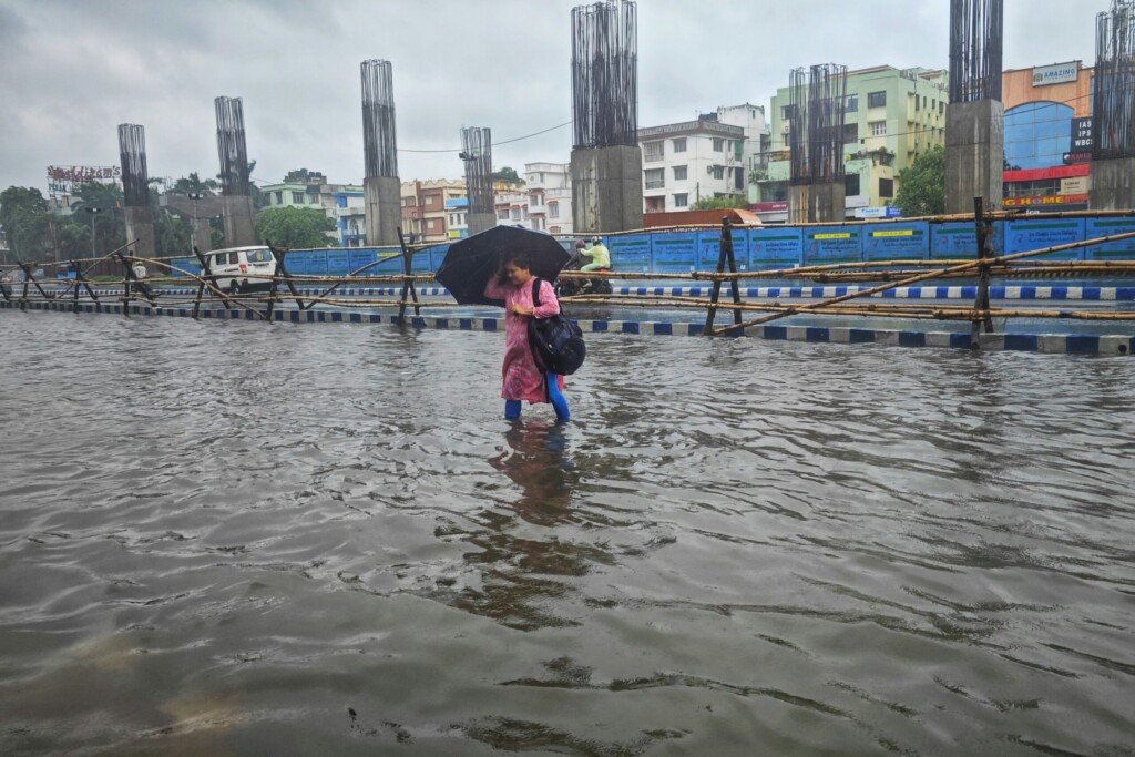 A person walking through a waterlogged Kolkata street with an umbrella during monsoon rain