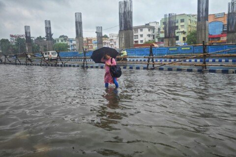 A person walking through a waterlogged Kolkata street with an umbrella during monsoon rain