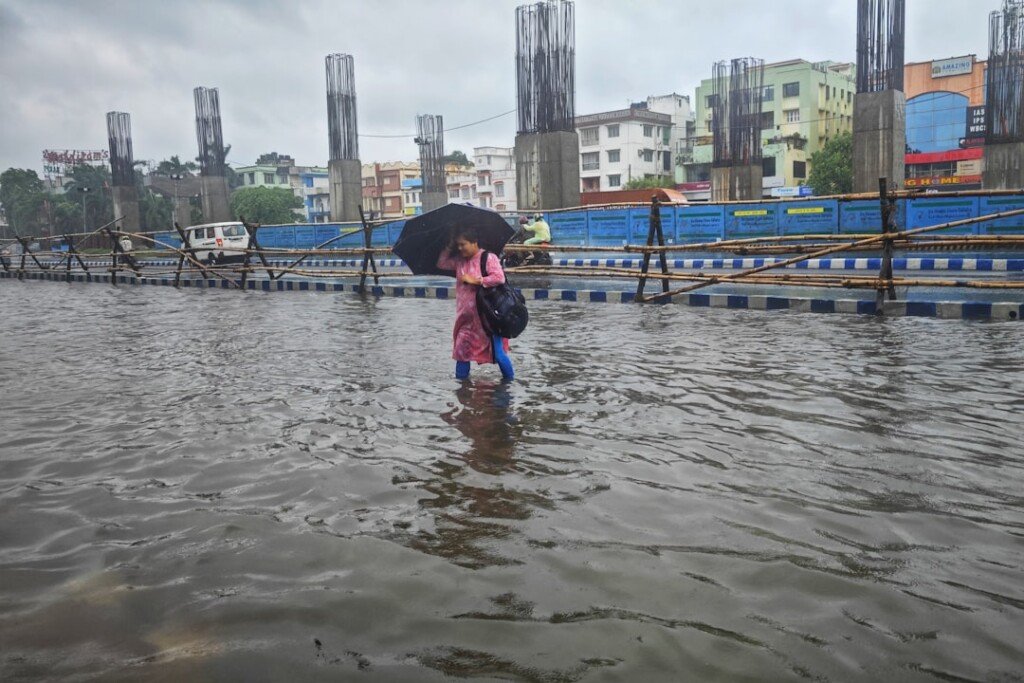 A person walking through a flooded Kolkata street with an umbrella during evening downpour