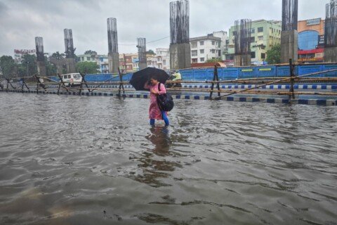 A person walking through a flooded Kolkata street with an umbrella during evening downpour