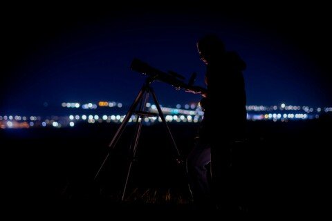 Person looking through a telescope at night with city lights in the background, illustrating National Space Day telescope viewing at BITM Kolkata