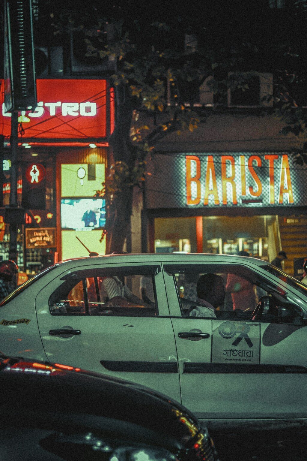 A taxi driving down Park Street, Kolkata at night with lit-up storefronts