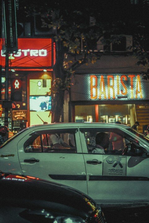 A taxi driving down Park Street, Kolkata at night with lit-up storefronts