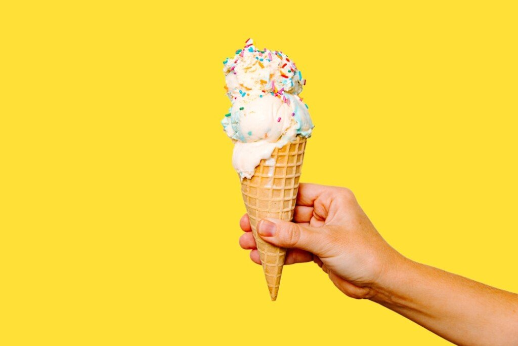Hand holding a scoop of ice cream in a cone, representing Kolkata's ice cream and kulfi shops