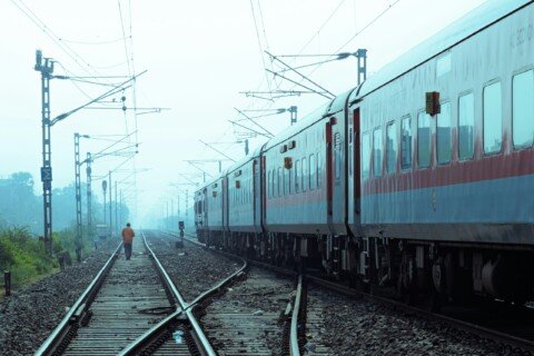 A man walking along an Indian railway track beside a stationary train