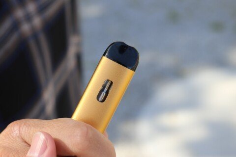 A person holding a yellow disposable vape e-cigarette device