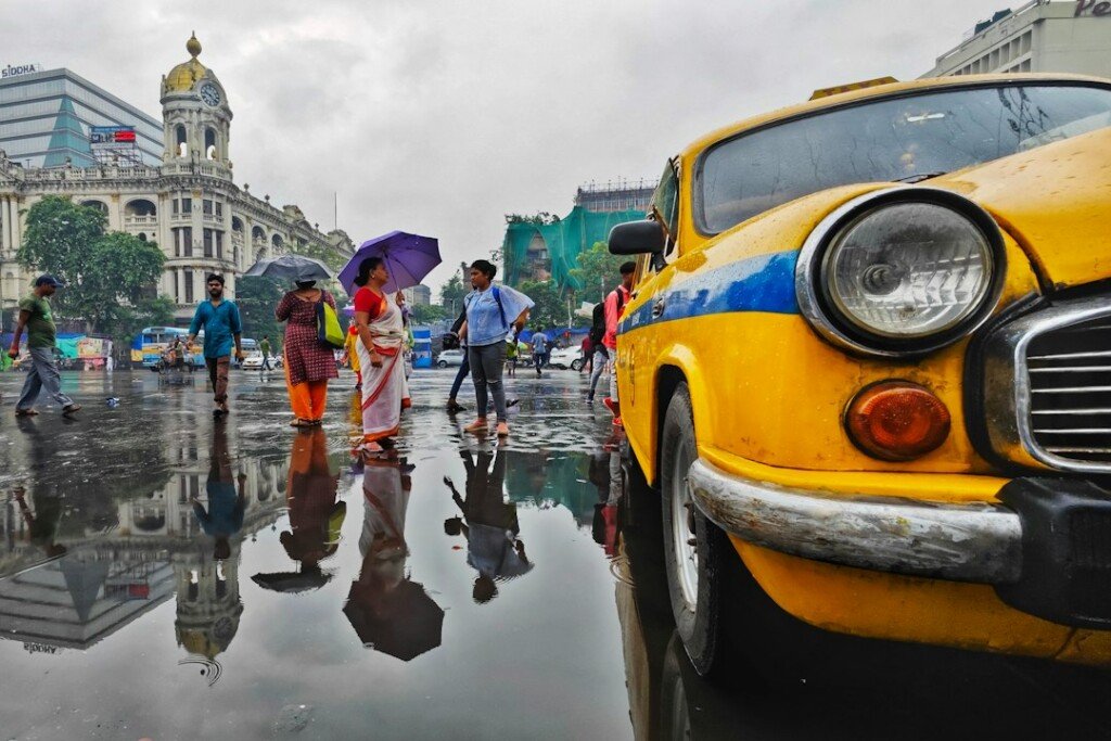 People with umbrellas walking through a Kolkata street in the rain