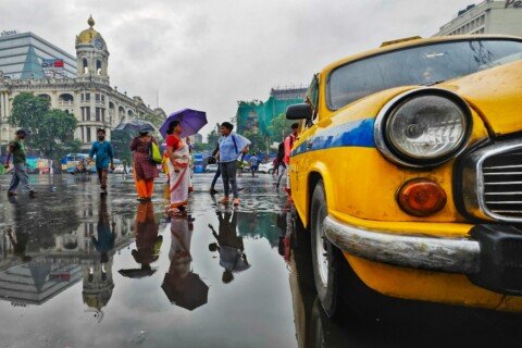 People with umbrellas walking through a Kolkata street in the rain