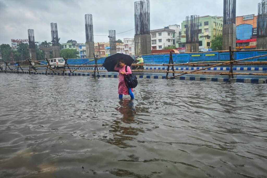 A person with an umbrella walking through a waterlogged Kolkata street in the rain