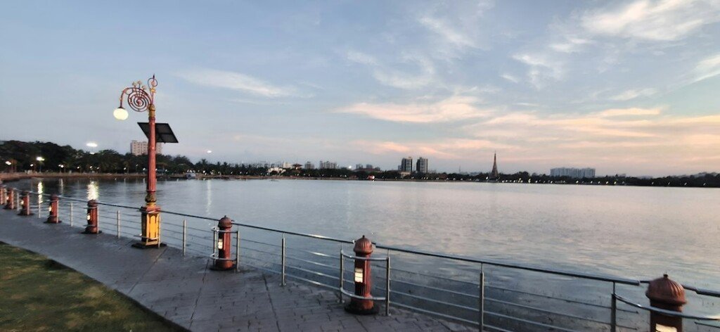 A calm lake surrounded by trees in a Kolkata park, with a walking trail along the water's edge