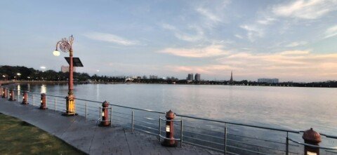A calm lake surrounded by trees in a Kolkata park, with a walking trail along the water's edge