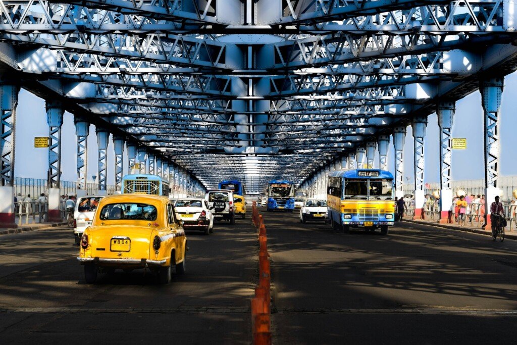 A yellow Kolkata taxi driving under Howrah Bridge, one of the main routes from Howrah station into the city