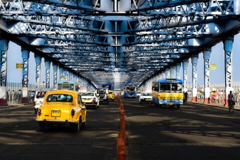 A yellow Kolkata taxi driving under Howrah Bridge, one of the main routes from Howrah station into the city