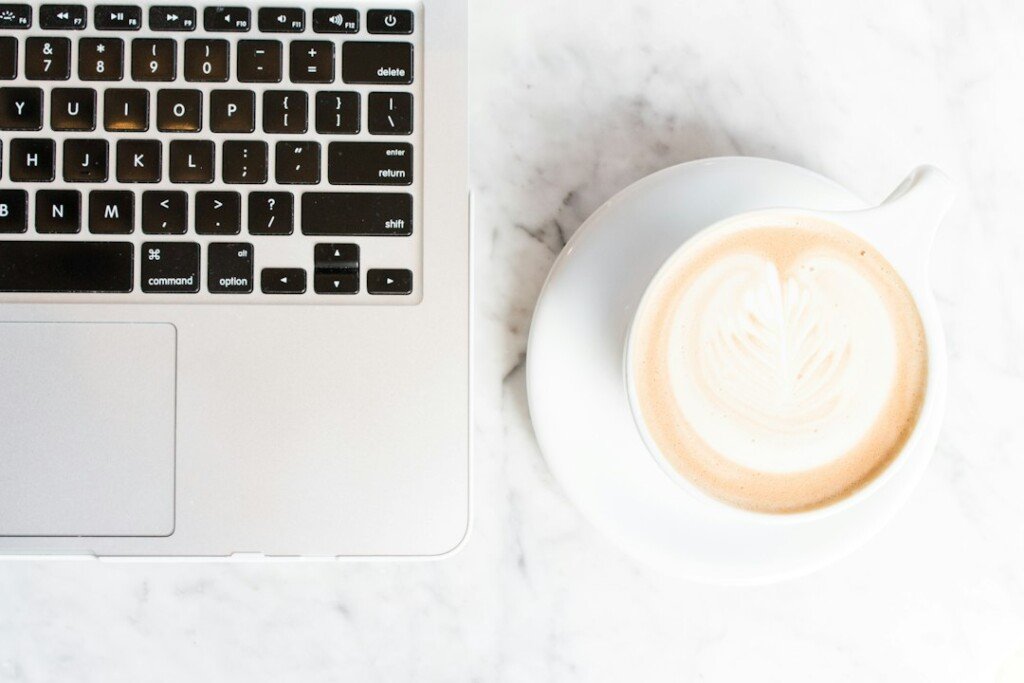 Cappuccino on a cup and saucer beside a laptop on a cafe table, a typical work-friendly cafe setup