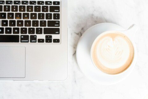 Cappuccino on a cup and saucer beside a laptop on a cafe table, a typical work-friendly cafe setup