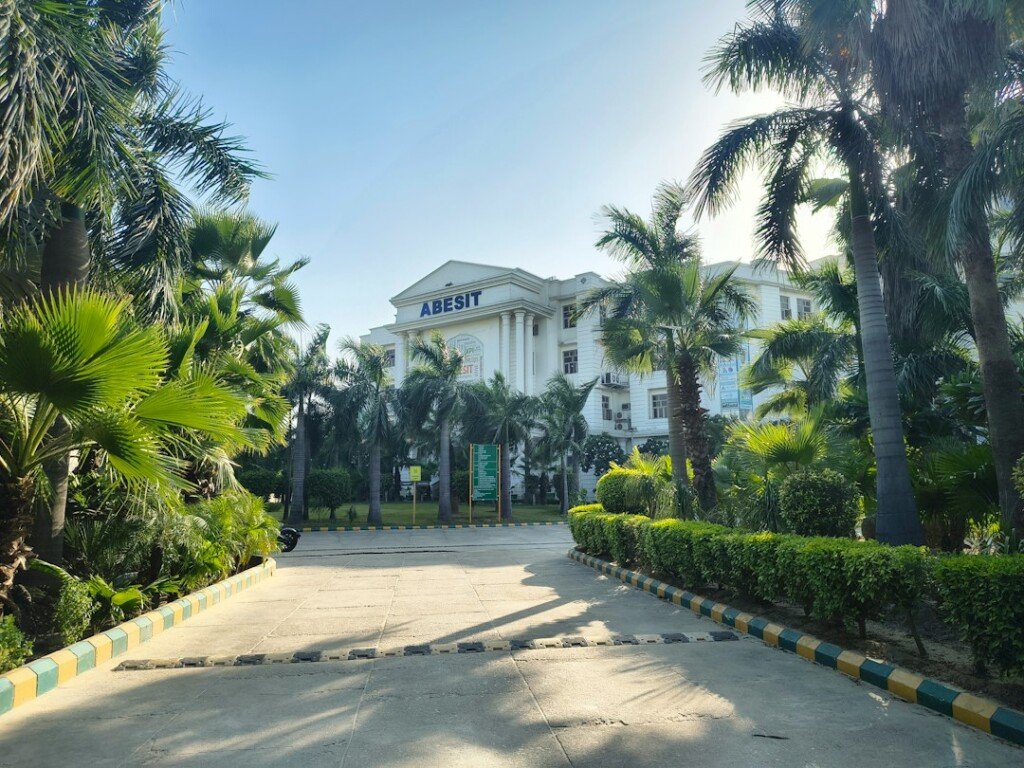 Grand college building entrance with palm trees and manicured hedges