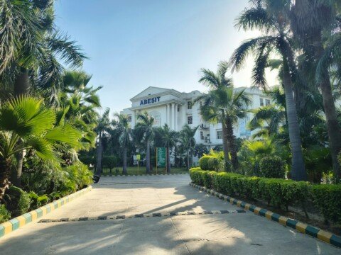 Grand college building entrance with palm trees and manicured hedges