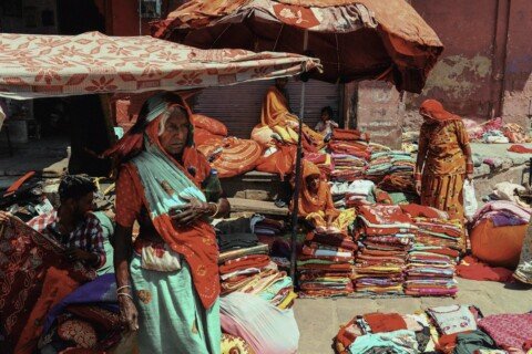 Piles of colourful folded cotton sarees and fabrics on display at an Indian textile market stall