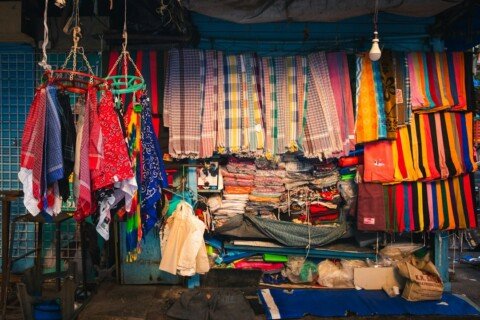 Colourful fabrics and festive goods on display at an Indian market stall, typical of Durga Puja shopping
