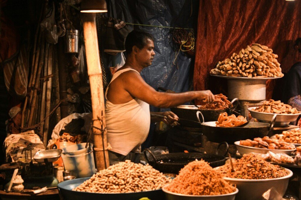 Street food vendor standing behind a table full of snacks at a Kolkata food stall