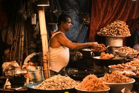 Street food vendor standing behind a table full of snacks at a Kolkata food stall