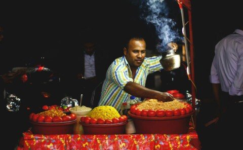 Street food vendor serving snacks at a busy roadside stall, typical of Kolkata street food